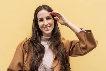 Smiling woman with long hair in front of yellow wall - DLTSF03300