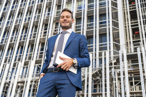 Lächelnder Geschäftsmann mit Tablet-PC vor einem Bürogebäude stehend - DLTSF03314