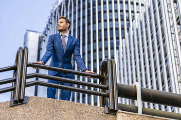 Nachdenklicher Geschäftsmann lehnt sich an ein Geländer vor einem Bürogebäude - DLTSF03322
