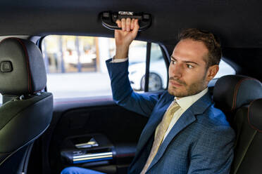 Businessman holding handle sitting in taxi - DLTSF03326