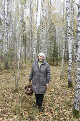 Lächelnde ältere Frau hält Korb mit Pilzen im Wald - EYAF02265