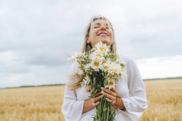 Lächelnde Frau steht mit Strauß weißer Blumen vor dem Himmel - MDOF00141
