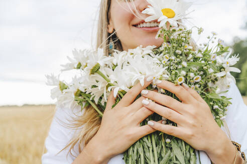 Glückliche Frau mit einem Strauß weißer Gänseblümchen auf einem Feld - MDOF00145