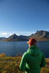 Woman wearing green padded jacket admiring Segla mountains on Senja island - AMNF00064