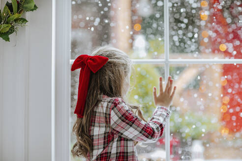 Girl with red ribbon in hair looking through window - MDOF00148