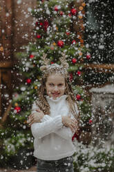 Lächelndes Mädchen steht unter Schneefall im Vorgarten - MDOF00151