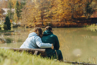 Frau umarmt Mann, der auf einer Bank vor einem See sitzt - OSF01102