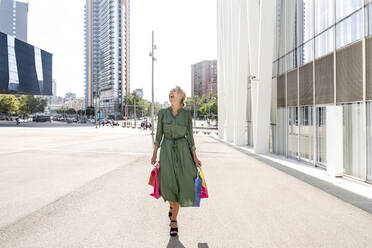 Ältere Frau mit Einkaufstüten lachend auf dem Fußweg in der Stadt - OIPF02492