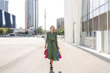 Mature woman with shopping bags laughing on footpath in city - OIPF02492