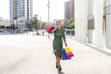Lächelnde reife Frau mit Einkaufstaschen an einem sonnigen Tag - OIPF02493