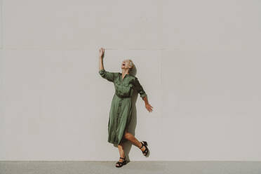 Mature woman laughing in front of white wall on sunny day - OIPF02505