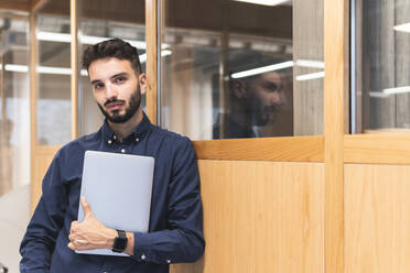 Geschäftsmann mit Laptop an der Wand lehnend - JAQF01086