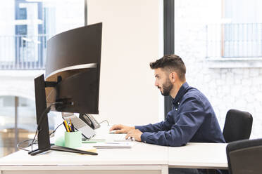 Young businessman working on laptop at desk in office - JAQF01089