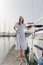 Happy young woman standing by boat on jetty - JRVF03134