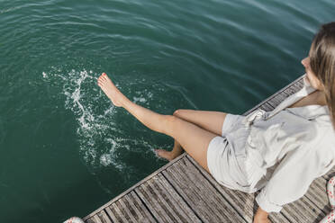 Junge Frau planscht mit den Füßen im Wasser am Steg - JRVF03143