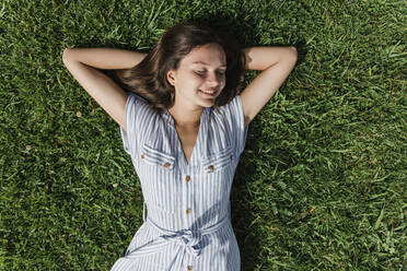 Happy young woman with eyes closed relaxing on grass - JRVF03150