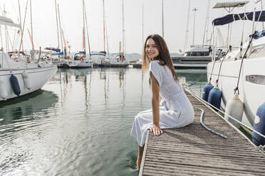 Glückliche junge Frau auf dem Bootssteg sitzend - JRVF03152