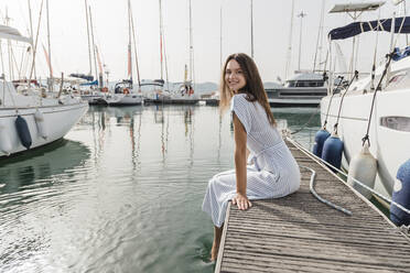 Happy young woman sitting on jetty - JRVF03152