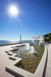 Italy, Friuli Venezia Giulia, Grado, Sun shining over modern promenade fountain - WWF06227