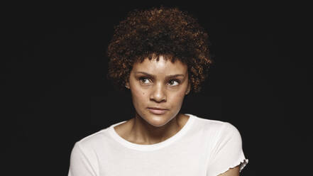 Portrait of a young woman isolated on black background. Close up of a curly haired woman looking away. - JLPSF17799