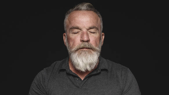 Nahaufnahme eines älteren Mannes mit weißem Bart und geschlossenen Augen. Portrait eines älteren Mannes mit geschlossenen Augen, isoliert auf schwarzem Hintergrund. - JLPSF17820