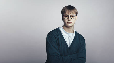 Young man wearing eyeglasses standing against grey background. Man standing with arms crossed looking at camera. - JLPSF17892