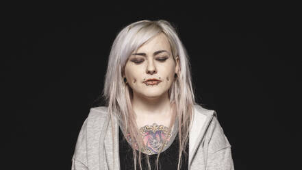 Woman with white hair and tattoo on body with her eyes closed. Woman with fashion piercing on lips and cheeks isolated on black background. - JLPSF17974