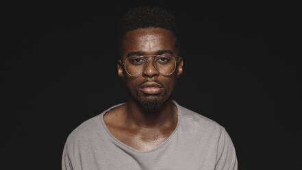 Afrikanischer Mann mit Brille und T-Shirt isoliert auf schwarzem Hintergrund. Nahaufnahme eines afrikanischen Mannes, der in die Kamera schaut. - JLPSF17988