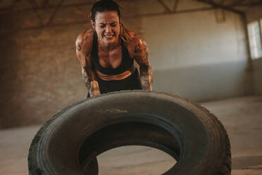 Fit weiblichen Athleten trainieren mit einem riesigen Reifen, Drehen und Flipping in Cross-Workout Raum. Frau, die mit großen Reifen in einem verlassenen Lagerhaus. - JLPSF18003