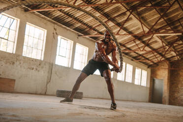 Fitness Mann übt mit Kampf Seil in verlassenen Lagerhalle. Starker Mann übt in Cross-Training Fitnessraum in alten Fabrik gemacht. - JLPSF18009