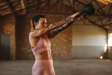 Frau trainiert mit Kettlebell in einem Cross-Trainingsraum. Fitness-Frau trainiert mit Kettlebell in einem alten Lagerhaus. - JLPSF18011