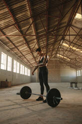 Muscular woman standing at gym with barbell on floor. Strong fitness female at gym inside old warehouse. - JLPSF18016