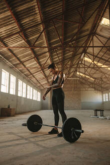 Muskulöse Frau steht im Fitnessstudio mit Langhantel auf dem Boden. Starke Fitness-Frau im Fitnessstudio in einem alten Lagerhaus. - JLPSF18016