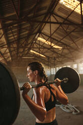 Fit Frau trainiert mit Langhantel mit schweren Gewichten in einer Turnhalle in leeren Lagerhalle. weibliche tun Kniebeugen Übung. - JLPSF18018