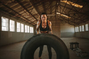 Starke Frau trainiert mit einem Reifen in einem Cross-Trainingsstudio in einem alten Lagerhaus. Muskulöse Frau trainiert mit einem großen Reifen. - JLPSF18022