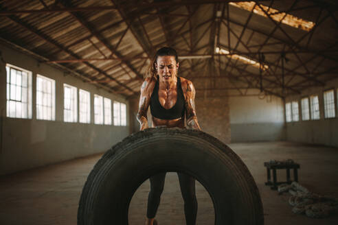 Strong woman exercising with a tire in cross training gym inside old warehouse. Muscular female working out with big tire. - JLPSF18022