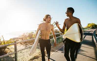 Lächelnde männliche Freunde, die mit Surfbrettern zum Strand gehen. Beste Freunde, die im Urlaub surfen gehen. - JLPSF18058