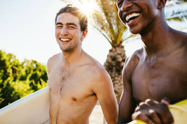 Lächelnder junger Mann, der mit einem Freund auf dem Wasser surft. Zwei junge Männer, die in ihrem Urlaub surfen gehen. - JLPSF18060