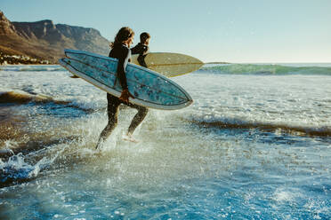 Zwei männliche Surfer, die zum Surfen ins Meer gehen. Zwei Männer mit Surfbrettern, die zum Surfen ins Meer laufen. - JLPSF18067