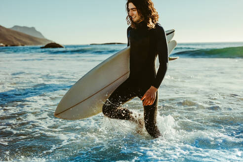 Junger Mann mit Surfbrett am Strand, der nach dem Surfen aus dem Meer kommt. - JLPSF18068