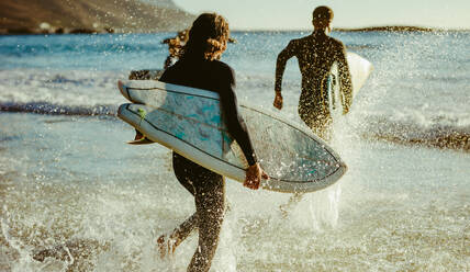 Rückansicht von zwei Männern, die mit Surfbrettern ins Meer gehen. Männliche Surfer, die zum Surfen ins Meer laufen. - JLPSF18069