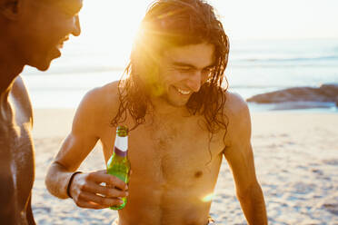 Lächelnder junger Mann beim Bier mit einem Freund am Strand. Zwei junge Männer mit Bier am Meer. - JLPSF18077