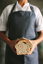 Ausschnitt einer Bäckerin in Uniform, die frisches Brot in der Hand hält. Eine Bäckerin hält einen Brotlaib in einer Bäckerei. - JLPSF18083