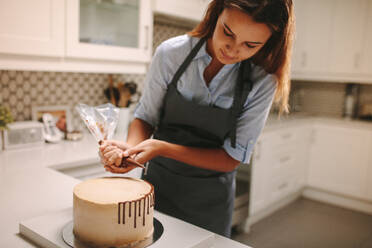 Konditorin dekoriert Kuchen mit Schokoladenglasur. Kuchen auf Küchentisch mit weiblicher Köchin, die ihn dekoriert. - JLPSF18103