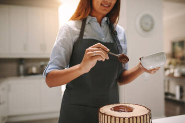 Frau gießt flüssige Schokolade auf den Kuchen zum Dekorieren. Weibliche Köchin bereitet leckeren Schokoladenkuchen in der Küche zu. - JLPSF18109