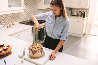 Köchin schneidet frisch zubereiteten Kuchen in der Küche an. Konditorin schneidet einen Kuchen an. - JLPSF18128