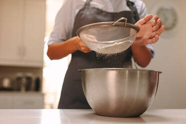 Nahaufnahme von weiblichen Konditorin Sieben Mehl in einer Schüssel zu machen Teig in der Küche. Frau Bäckerin Backen in der Küche zu Hause. - JLPSF18139