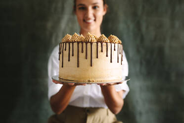 Eine Bäckerin hält einen leckeren Kuchen in der Hand, ein Koch hält einen frisch gebackenen Kuchen vor grauem Hintergrund. - JLPSF18151