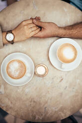 Top view of hands of man and woman held together in expression of love. Close up of man holding hand of a woman on a table with cups of coffee by the side. - JLPSF18161