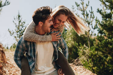Man carrying girlfriend on his back while walking on a mountain trail. Couple enjoying themselves on a mountain trail. - JLPSF18166